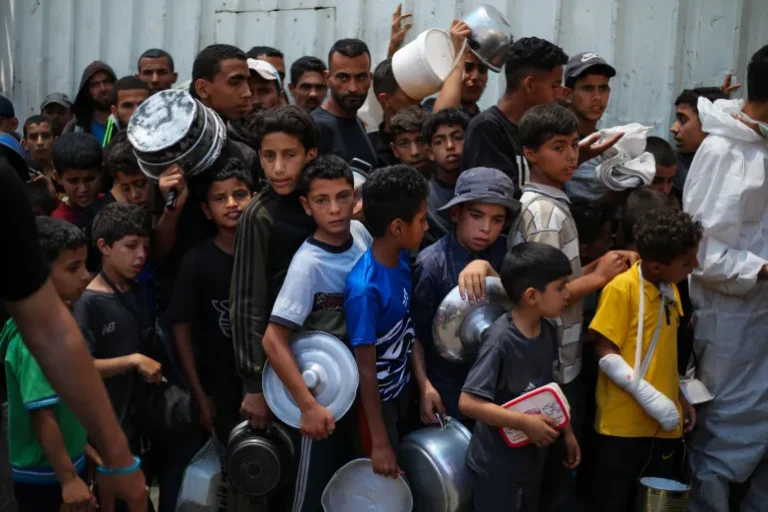 Anak-anak Palestina menunggu bersama anak-anak lain untuk mendapatkan makanan di titik distribusi di Nuseirat, Gaza tengah [File: Eyad Baba/AFP]