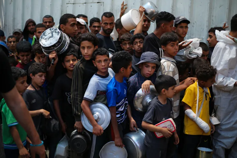 Anak-anak Palestina menunggu bersama anak-anak lain untuk mendapatkan makanan di titik distribusi di Nuseirat, Gaza tengah [File: Eyad Baba/AFP]