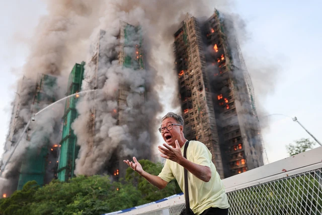 Seorang pria bereaksi saat asap mengepul sementara api melahap perancah bambu di beberapa gedung di perumahan Wang Fuk Court, Tai Po, Hong Kong, Rabu (26/11/2025). Foto: Tyrone Siu/REUTERS