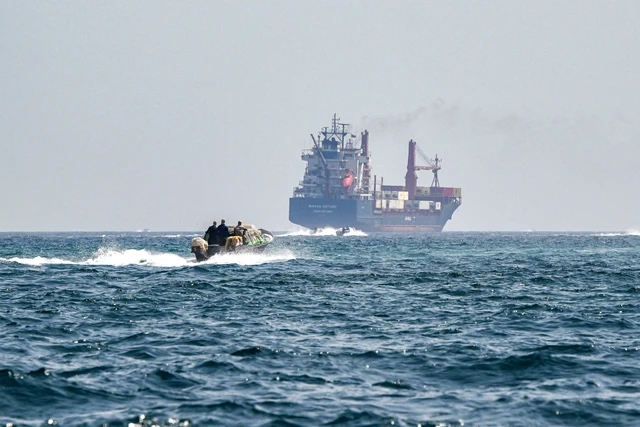 Sebuah perahu mendekati kapal kontainer Marsa Victory berbendera St Kitts dan Nevis saat berlayar di perairan Selat Hormuz di lepas pantai Khasab di semenanjung Musandam utara Oman pada 25 Juni 2025. Foto: Giuseppe Cacace/AFP